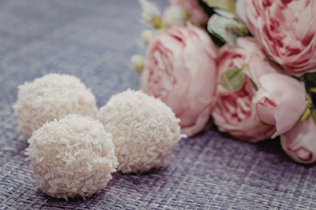 Three coconut treats placed on a purple surface with a bouquet of pink flowers in the background