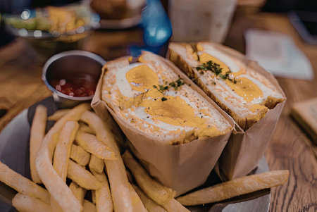 A mouthwatering breakfast sandwich cut in half, served with a side of crispy fries and a dipping...