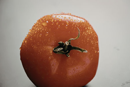 A close-up image of a single, ripe red tomato with water droplets on its surface.