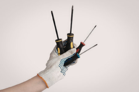 A hand wearing a white glove holding multiple screwdrivers with different tips and handles.