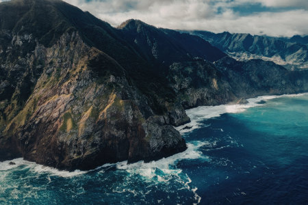 A breathtaking aerial view of rugged cliffs and mountains meeting the ocean under a cloudy sky.