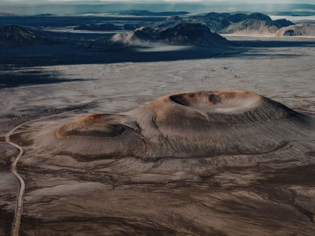 Aerial view of a vast mountainous terrain with a winding dirt road and rugged hills