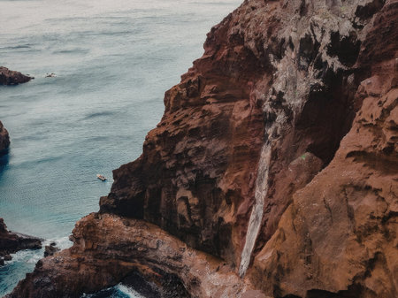 A breathtaking aerial view of a waterfall flowing down a rocky cliff into the sea, surrounded by...