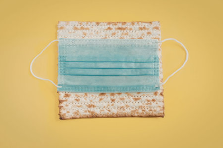 A matzo bread with a blue face mask on it, set against a bright yellow background.