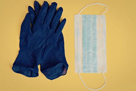A pair of blue medical gloves and a surgical face mask on a yellow background.の写真素材
