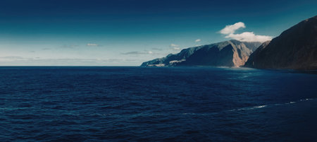 A serene landscape of a vast ocean meeting a mountain range under a clear blue sky with a few...