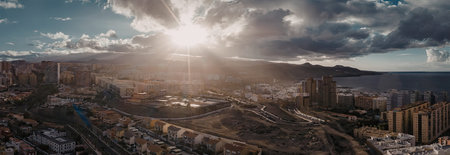 A panoramic view of a cityscape with a dramatic sky, featuring a mix of buildings, mountains, and a...