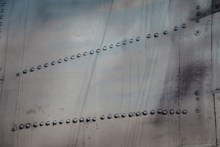 The image shows a close-up view of a metal sheet with two rows of rivets, showcasing industrial...