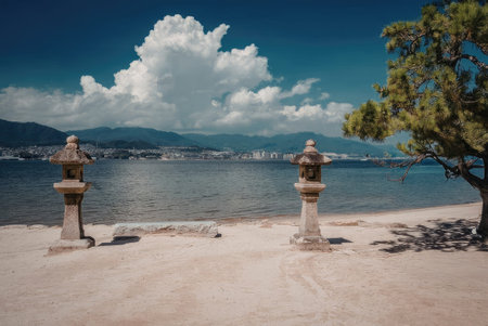 a serene beach scene featuring two stone lanterns on the sandy shore, with a tree to the right and a...