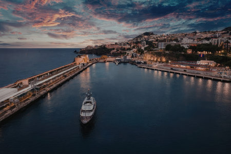 A tranquil harbor scene at dusk with a boat moored near a long pier, surrounded by buildings on the...
