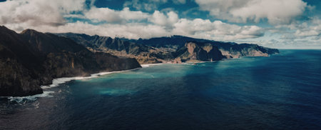 A tranquil ocean scene with a mountainous coastline under a blue sky with clouds.