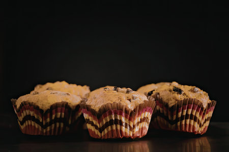 A close-up shot of three muffins with colorful wrappers on a dark background