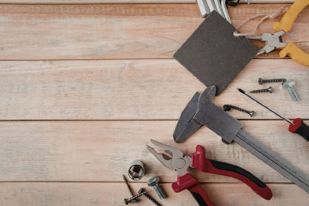 A selection of tools including pliers, screwdrivers, nails, and a wrench are laid out on a wooden...