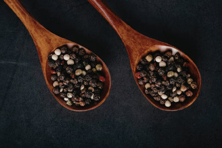 Two wooden spoons filled with a variety of colorful peppercorns on a dark background