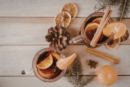 Two mugs of spiced orange drink on a wooden table with cinnamon sticks and dried orange slices