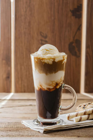 A layered affogato coffee drink in a tall glass mug with a handle, placed on a wooden table with...