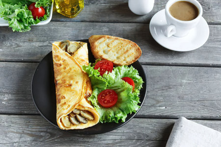 A plate of food with a crepe, toast, and salad on a wooden table with a cup of coffee