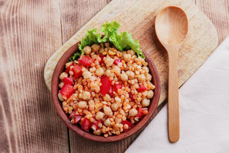 A bowl of chickpea salad with lettuce and tomatoes on a wooden tableの写真素材