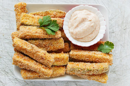 A plate of crispy breaded sticks served with a side of creamy dipping sauce, garnished with fresh...
