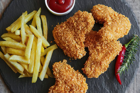 A plate of crispy fried chicken pieces and golden fries served with ketchup and chili pepper on a...