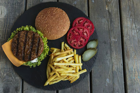 A mouth-watering burger with a beef patty, lettuce, cheese, and toppings, served with a side of crispy fries on a black plate.の写真素材