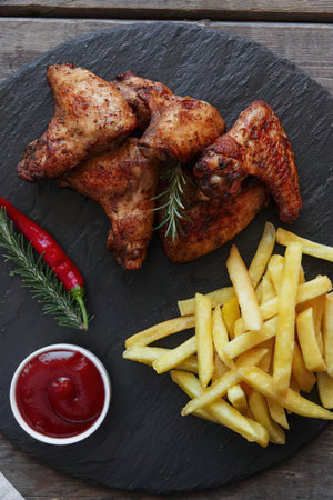 A plate of roasted chicken wings, crispy fries, and a side of ketchup, garnished with rosemary and...