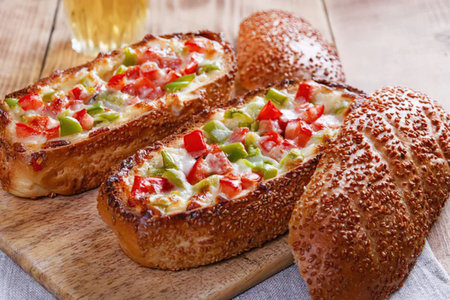 The image shows three pieces of bread, two of which are topped with cheese, red and green peppers,...