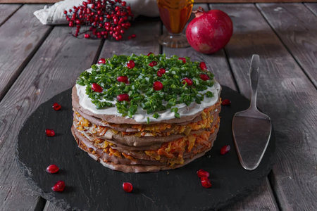 A layered salad with fresh greens, vegetables, and a creamy topping, presented on a black slate...