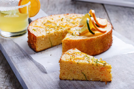 A sliced orange cake with zucchini and a glass of juice on a wooden board