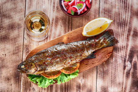 A grilled fish on a wooden plate with lemon, lettuce, tomato and a glass of beer