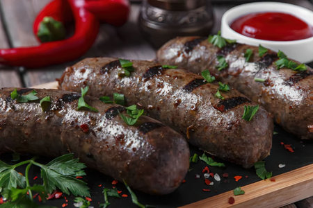 A plate of grilled meatballs garnished with fresh herbs and spices, served with a side of red sauce...