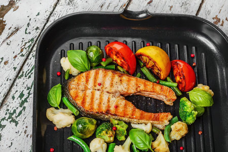 A grilled salmon fillet with vegetables in a black pan on a rustic wooden table