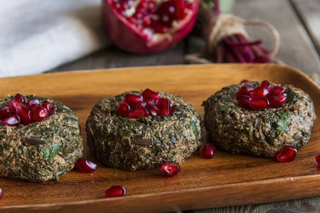 Three round meatballs made with herbs and topped with pomegranate seeds on a wooden serving tray,...