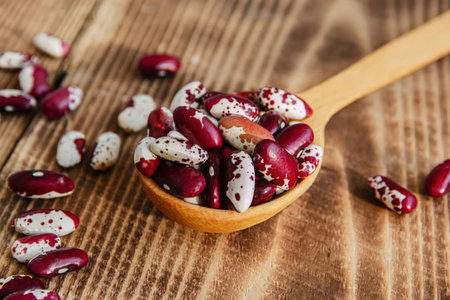 A wooden spoon filled with red and white kidney beans on a wooden surfaceの写真素材