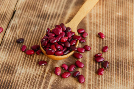 A wooden spoon filled with red beans on a wooden surface