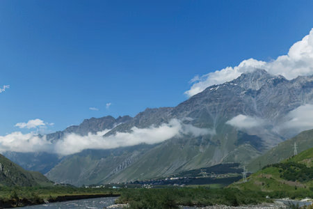 A scenic view of a mountain range with clouds and a river in the foreground.