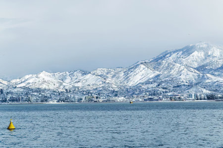 A serene landscape of snow-capped mountains meeting the sea, with a yellow buoy floating in the...
