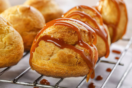 A close-up view of caramel profiteroles on a cooling rack, with a focus on the golden brown pastry...