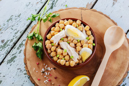 A bowl of chickpea salad with lemon wedges and herbs on a wooden plateの写真素材