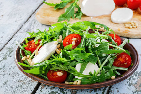 A delicious and healthy salad made with fresh arugula, cherry tomatoes, and mozzarella cheese.の写真素材