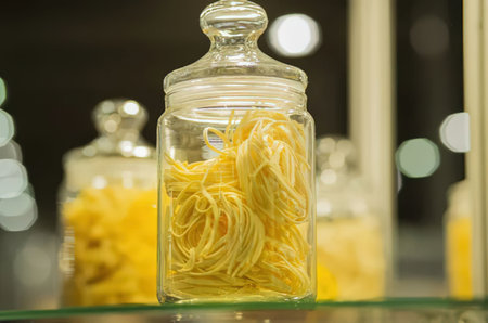 A glass jar filled with yellow noodles sits on a shelf with other jars in the background.の写真素材