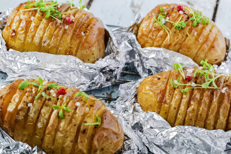 Four hasselback potatoes topped with herbs and chili flakes, wrapped in foil.
