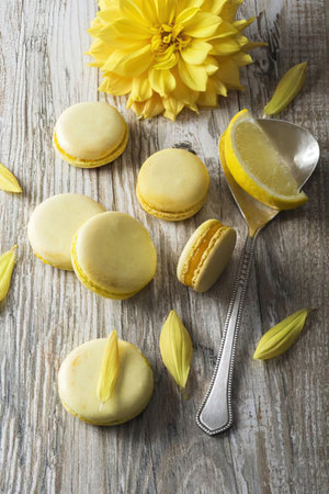 Delicious lemon macarons arranged on a wooden table with fresh yellow flowers and lemon slices.の写真素材
