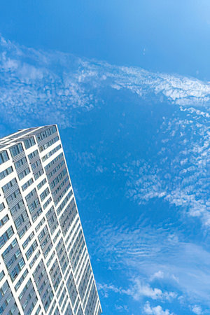 A tall building with many windows stands against a bright blue sky with scattered clouds.