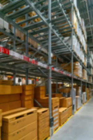 The image shows a blurry view of a warehouse aisle with shelving units on the right and stacked wooden crates on the left. The shelving units are made of metal and have multiple levels of storage. The wooden crates are stacked on top of each other and appear to be made of light-colored wood.の写真素材