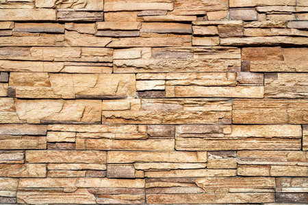 A close-up view of a brown stacked stone wall with various shades of brown and tan, featuring...