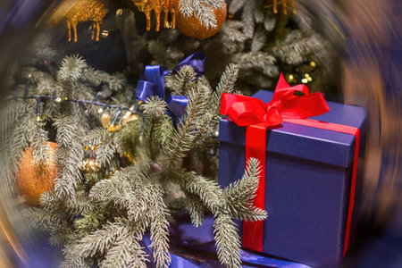 A blue gift box with a red ribbon sits under a Christmas tree, surrounded by branches and ornaments.の写真素材