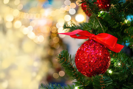 A close-up view of a Christmas tree with a red ornament and ribbon, set against a blurred background...