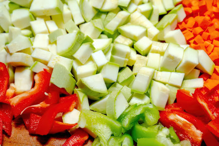 A close-up of chopped vegetables including red and green peppers, carrots, and zucchini on a cutting board.の写真素材