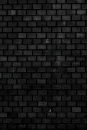 A close-up of a dark brick wall with rectangular bricks arranged in a staggered pattern, giving a sense of texture and depth.の写真素材